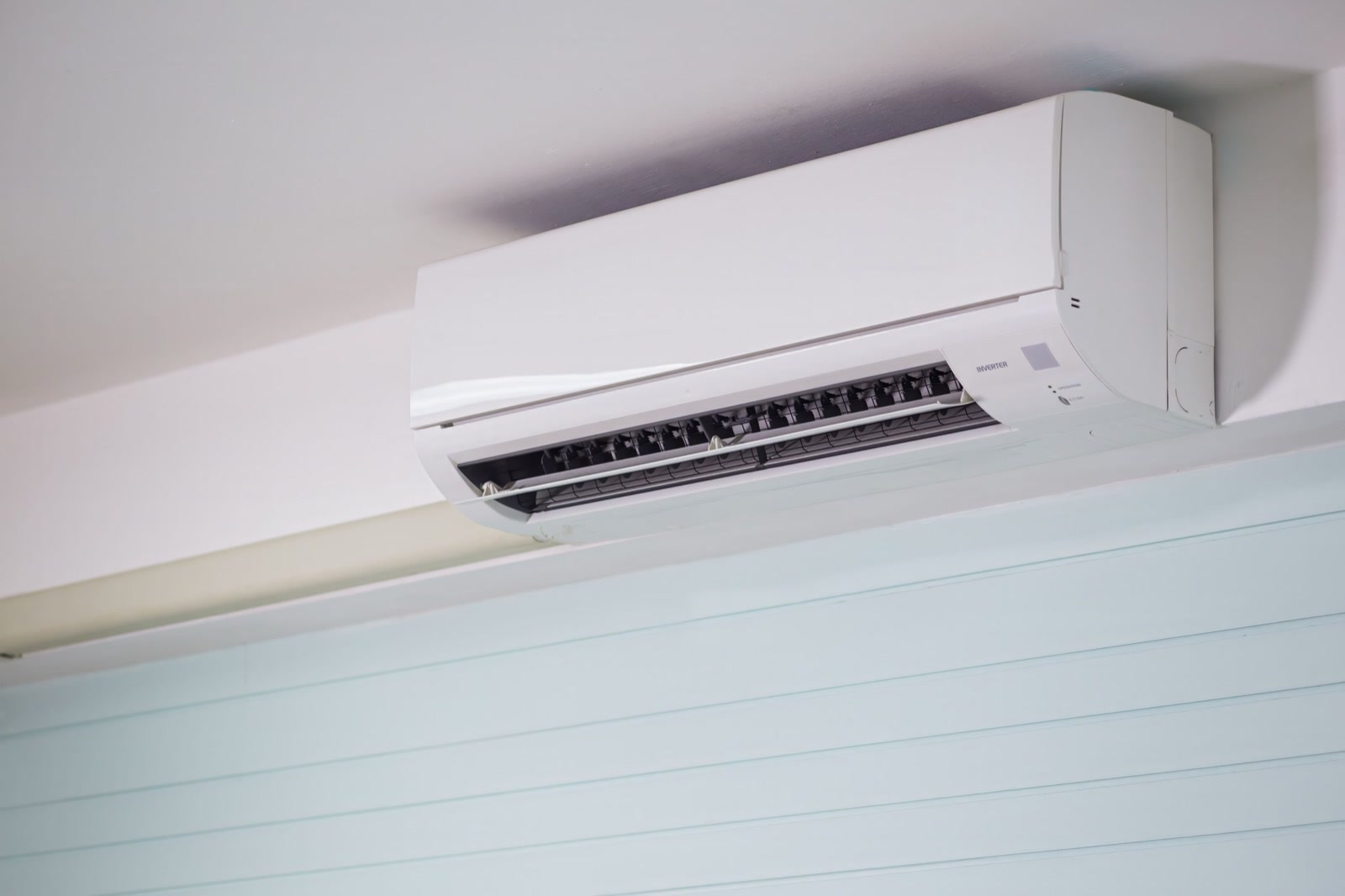 A white wall-mounted split air-conditioner fixed high on the wall of a room, its louvres open