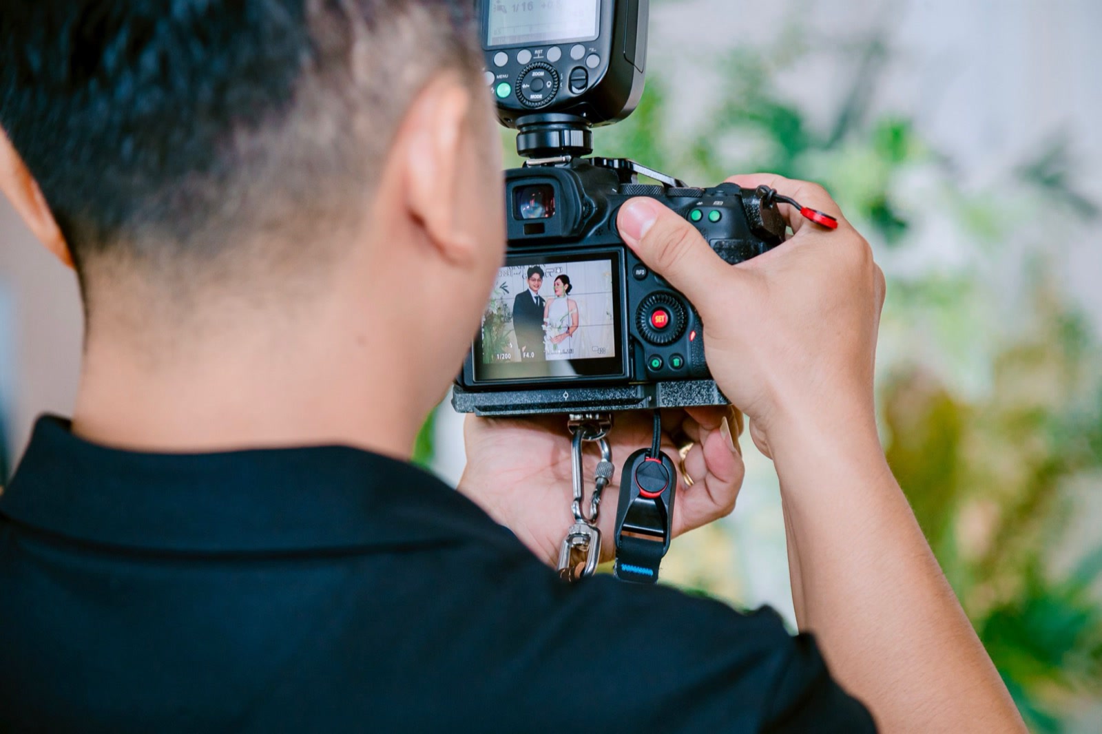 A photographer seen from behind, holding up a camera whose screen shows a bride and groom